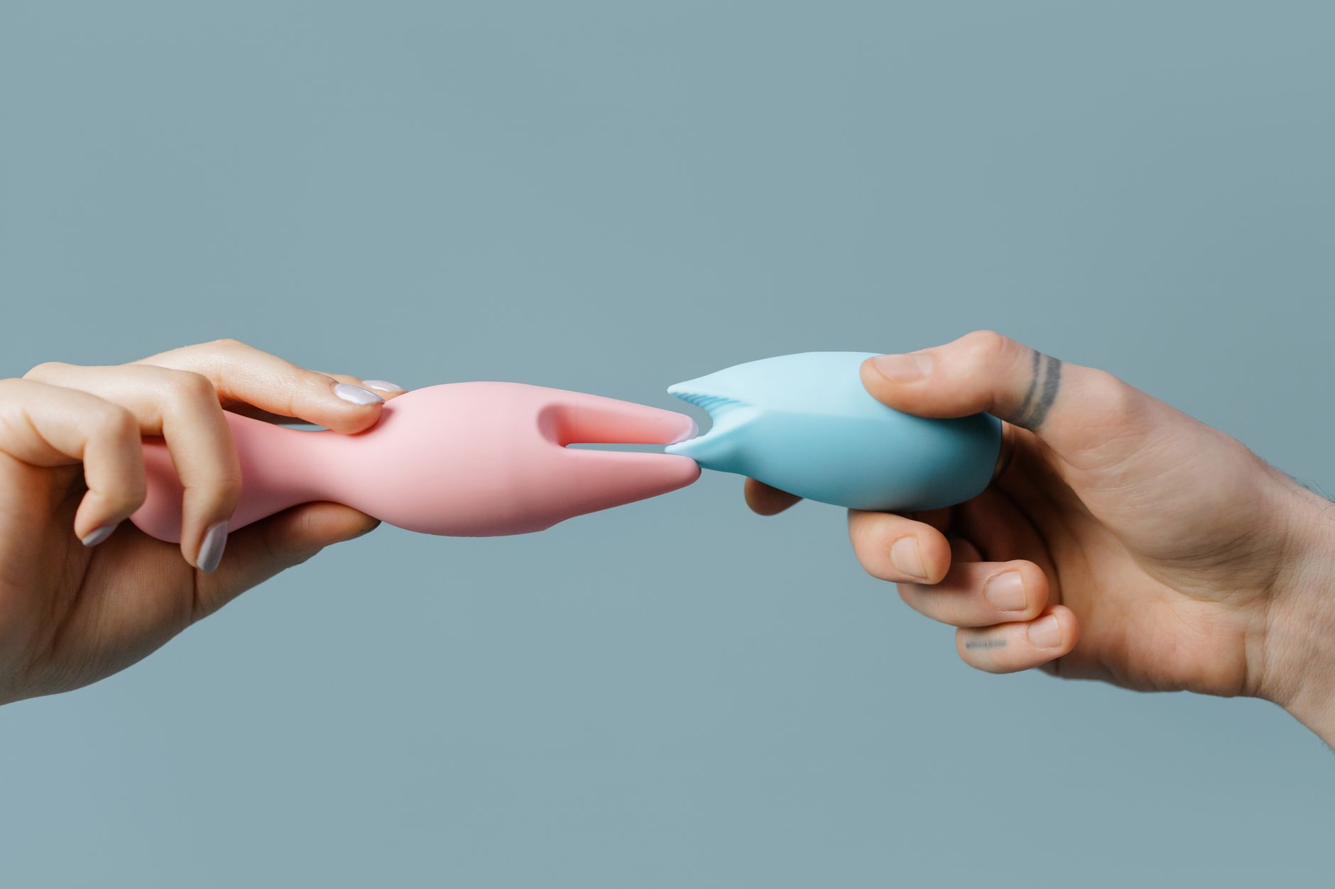 Hands holding pastel-colored silicone toys in a gentle, intimate gesture.